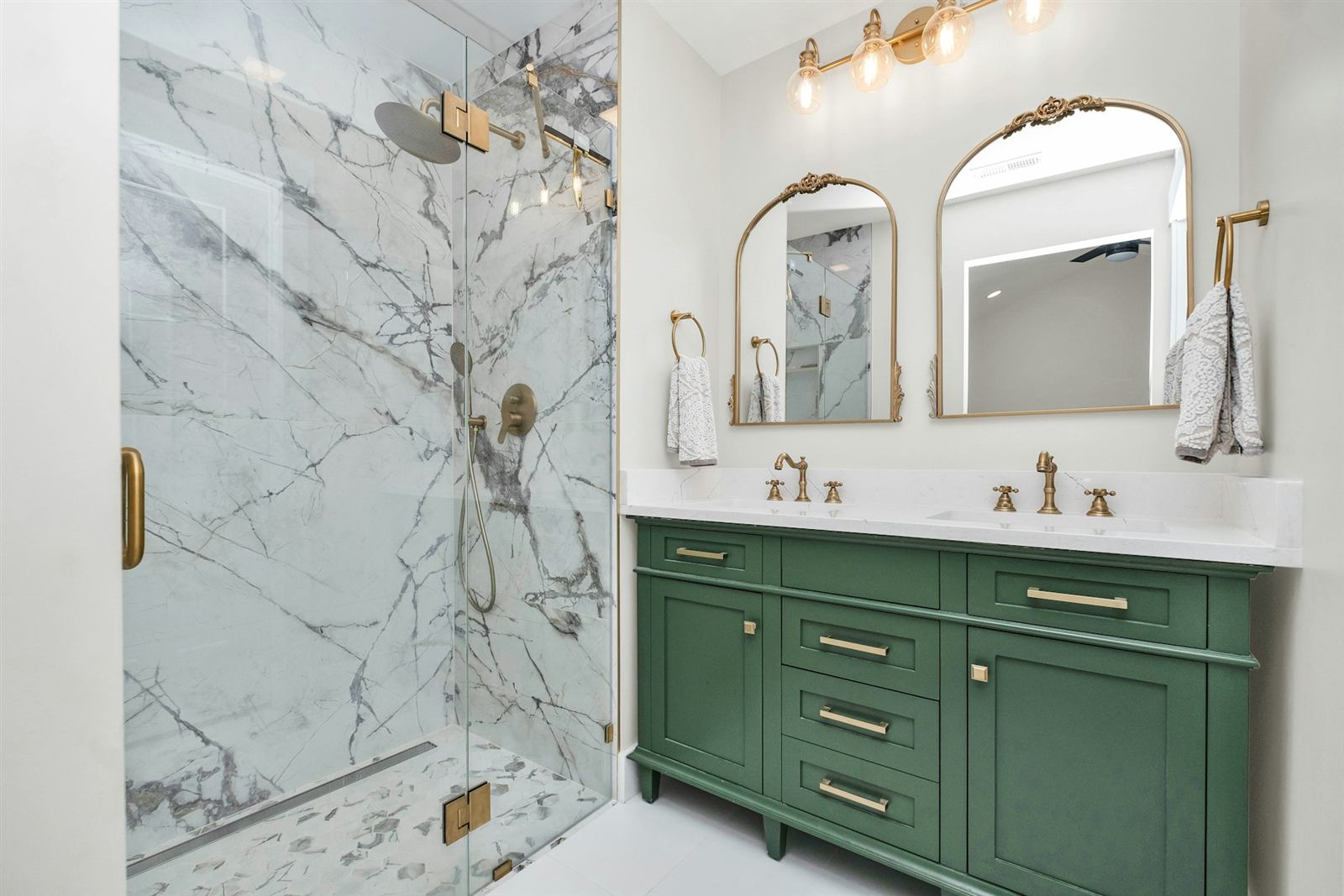Salle de bain avec meuble vert, miroirs en arche et douche en marbre